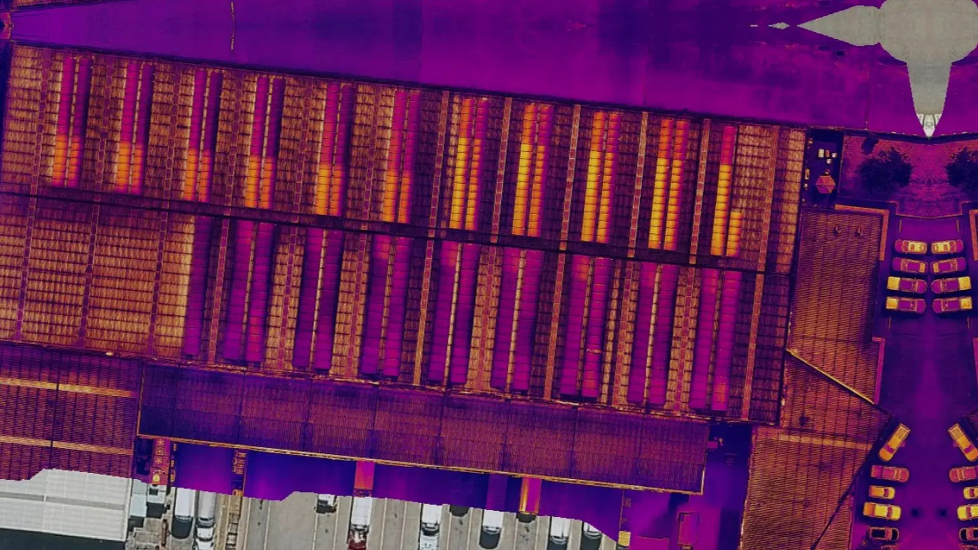 Thermal view of a Brisbane warehouse roof with commercial solar: warm panel strings show in orange and yellow against a purple roof.